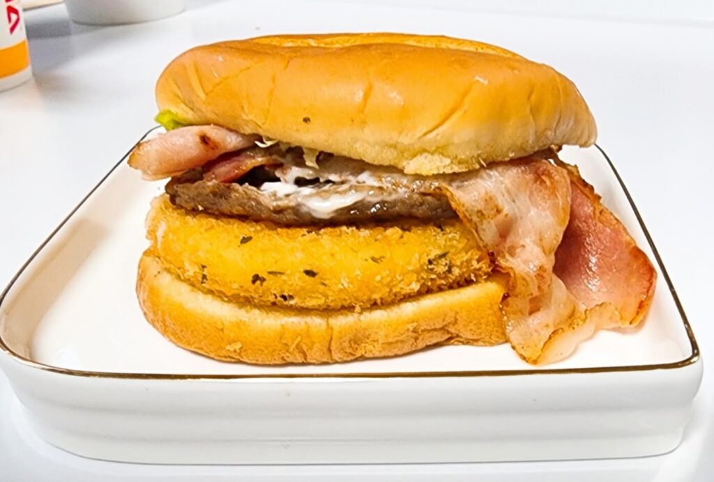 롯데리아 모짜렐라 인더버거 베이컨의 전체 구성 비주얼, 베이컨·치즈·패티가 보이는 햄버거 이미지