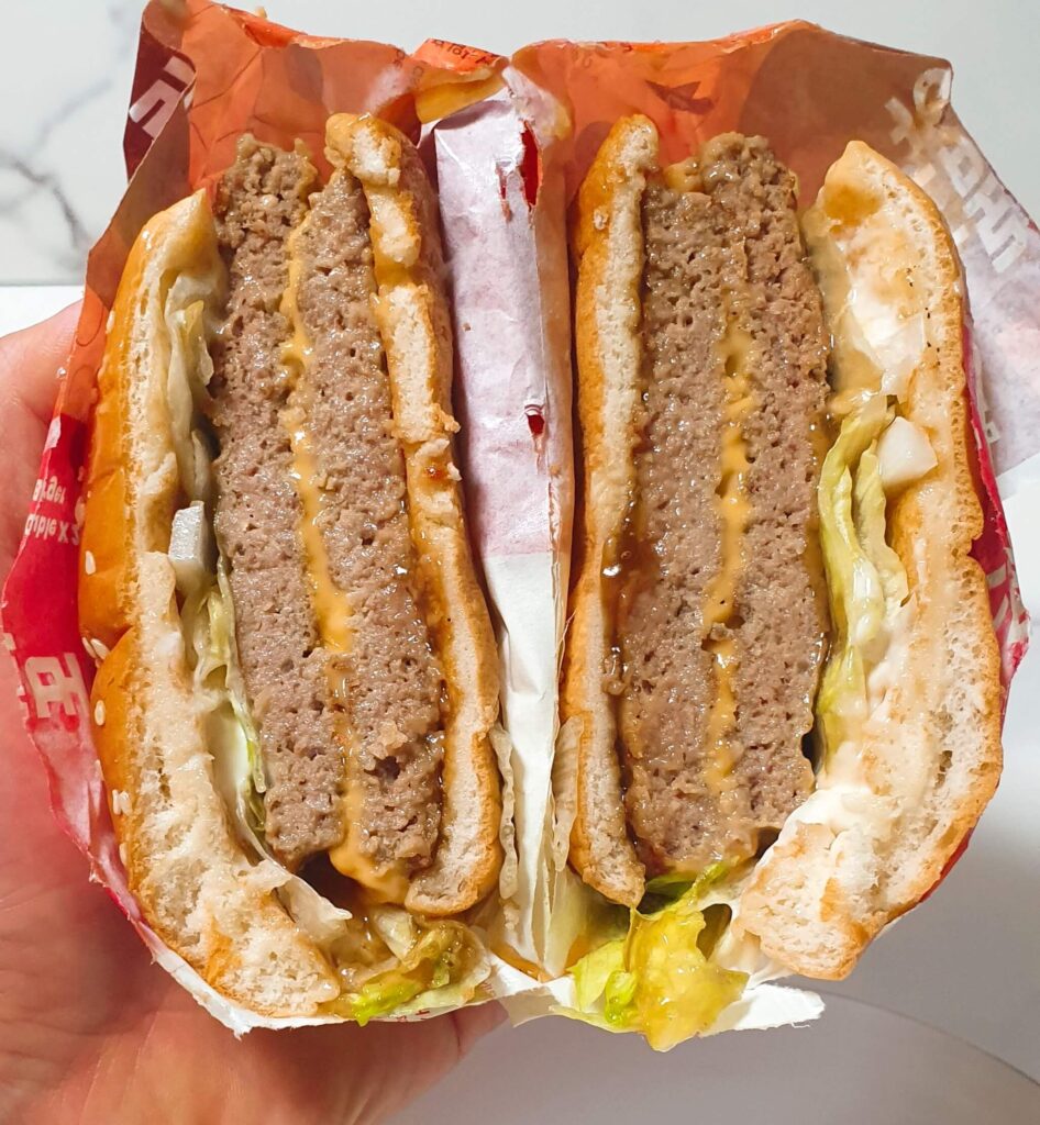 롯데리아 빅불 버거를 반으로 갈라 내부 구성을 확인한 사진. 두툼한 불고기 패티 두 장과 그 사이 녹아든 체다치즈의 완벽한 비율을 통해, 맛의 깊이와 양의 만족감을 동시에 충족하는 '만족스러운 선택'임을 증명하는 결론 이미지.