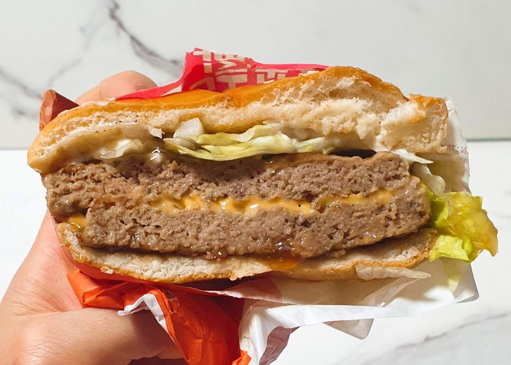 손으로 들어 올린 빅불 버거의 묵직한 단면 근접 사진. 결이 살아있는 더블 패티와 진한 소스의 조화를 시각화하여, 확실한 고기 맛을 원하는 독자들에게 빅불이 왜 '확실한 정답'인지를 보여주는 최종 결론 이미지.