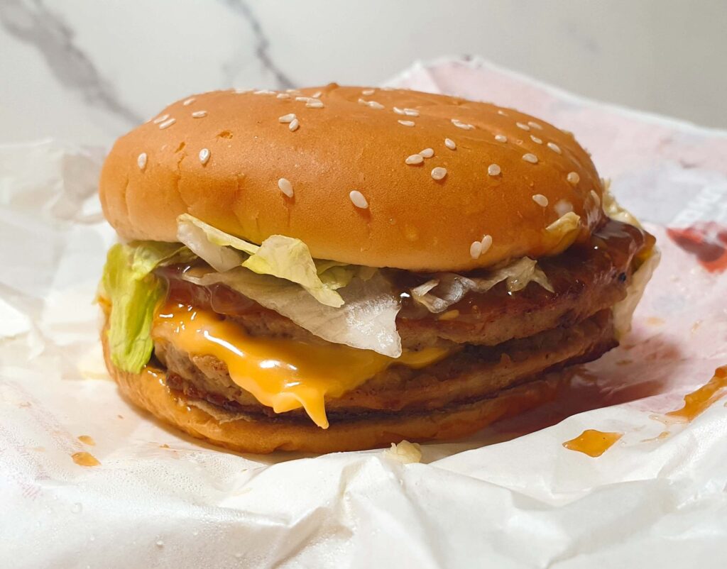 롯데리아 빅불의 뜨거운 더블 패티 사이로 부드럽게 녹아내린 노란 체다치즈의 실물 근접 사진. 불고기 소스와 치즈의 고소함이 어우러져 맛의 깊이를 더하는 모습을 시각적으로 보여주는 한끼도감 리뷰 이미지.