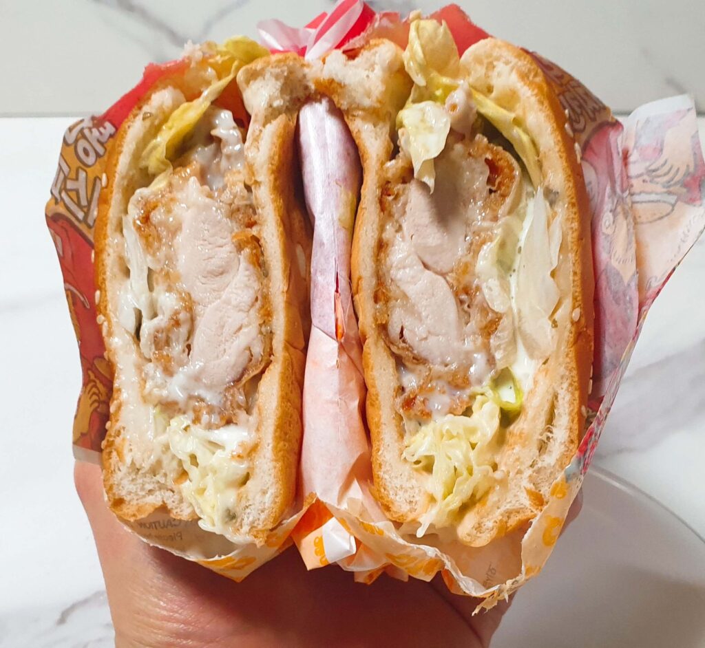 롯데리아 신메뉴 통다리 크리스피치킨버거 그릭랜치를 반으로 잘라 두툼한 통닭다리살 패티와 상큼한 화이트 소스의 조화를 보여주는 단면 상세 사진