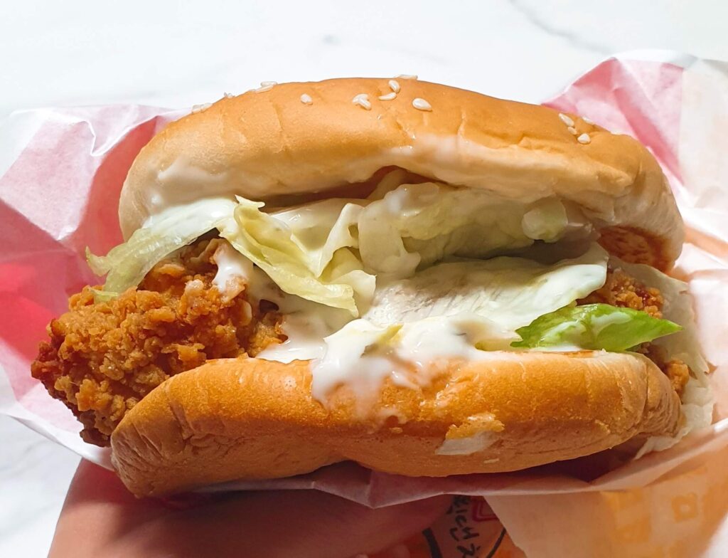 상큼하고 고소한 하얀색 그릭랜치 소스가 곁들여진 롯데리아 통다리 크리스피치킨버거 그릭랜치의 담백하고 바삭한 패티와 신선한 양상추 실물 사진