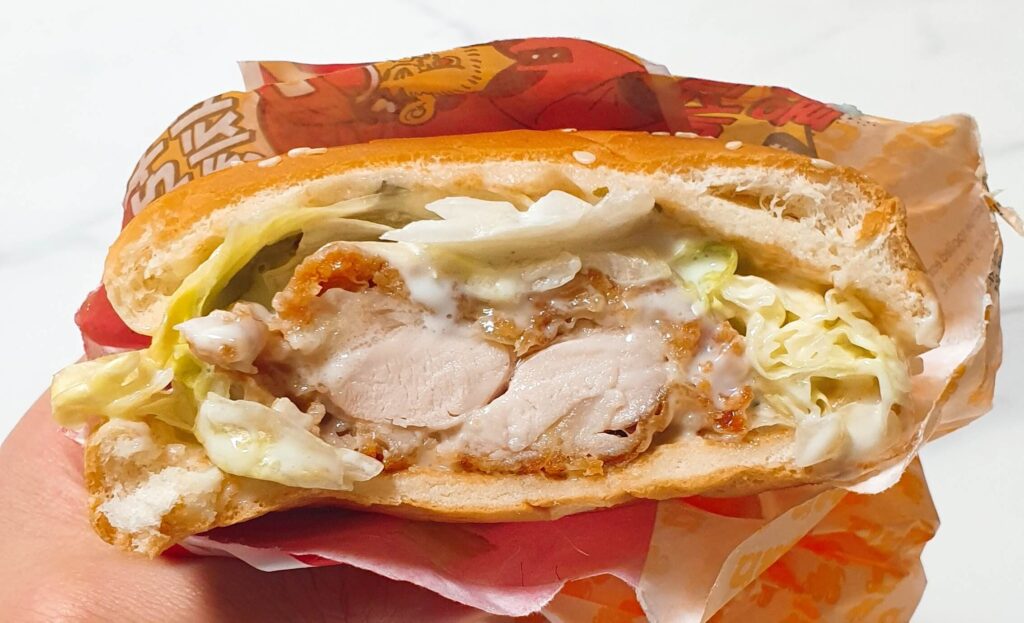 닭다리살의 결이 그대로 드러나는 롯데리아 통다리 크리스피치킨버거 그릭랜치의 패티 단면. 바삭한 튀김옷과 부드럽고 퍽퍽한 부위가 공존하는 실물 질감 이미지