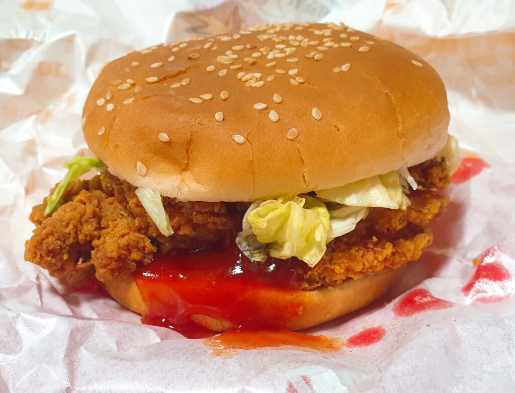 매콤하고 강렬한 레드 소스가 듬뿍 발라진 롯데리아 신메뉴 통다리 크리스피치킨버거 파이어핫의 바삭한 패티 모습