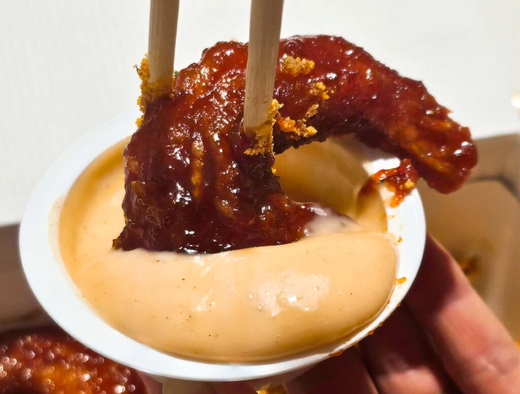 천년닭강정 전용 어니언 소스에 새우강정을 듬뿍 찍어 먹는 실물 사진. 느끼함을 잡아주는 소스와의 완벽한 궁합을 보여주며 실패 없는 맛 조합을 제안하는 이미지.